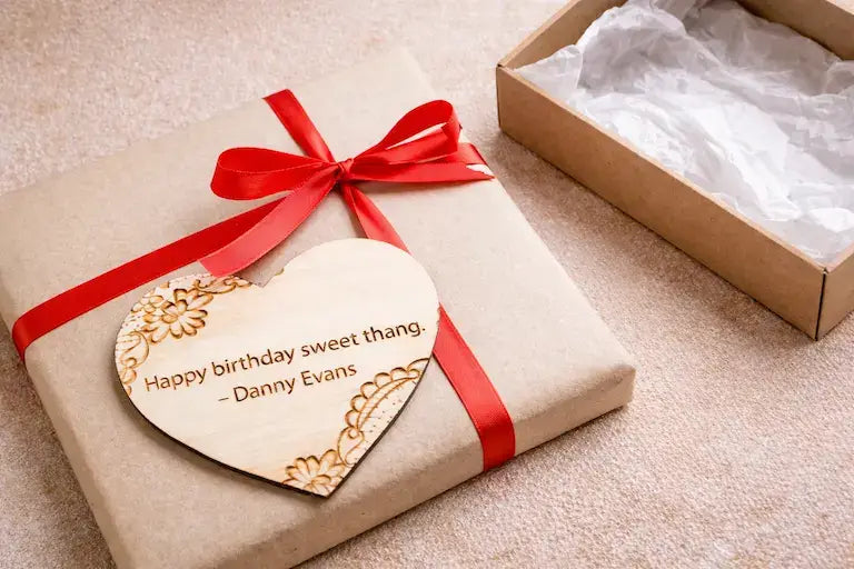 Close-up of rustic gift wrap with kraft paper, a red ribbon, and a personalized engraved wooden heart tag.
