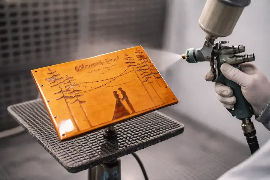 Artisan applying a protective finish to a custom laser-engraved wooden wedding guest book in the workshop.