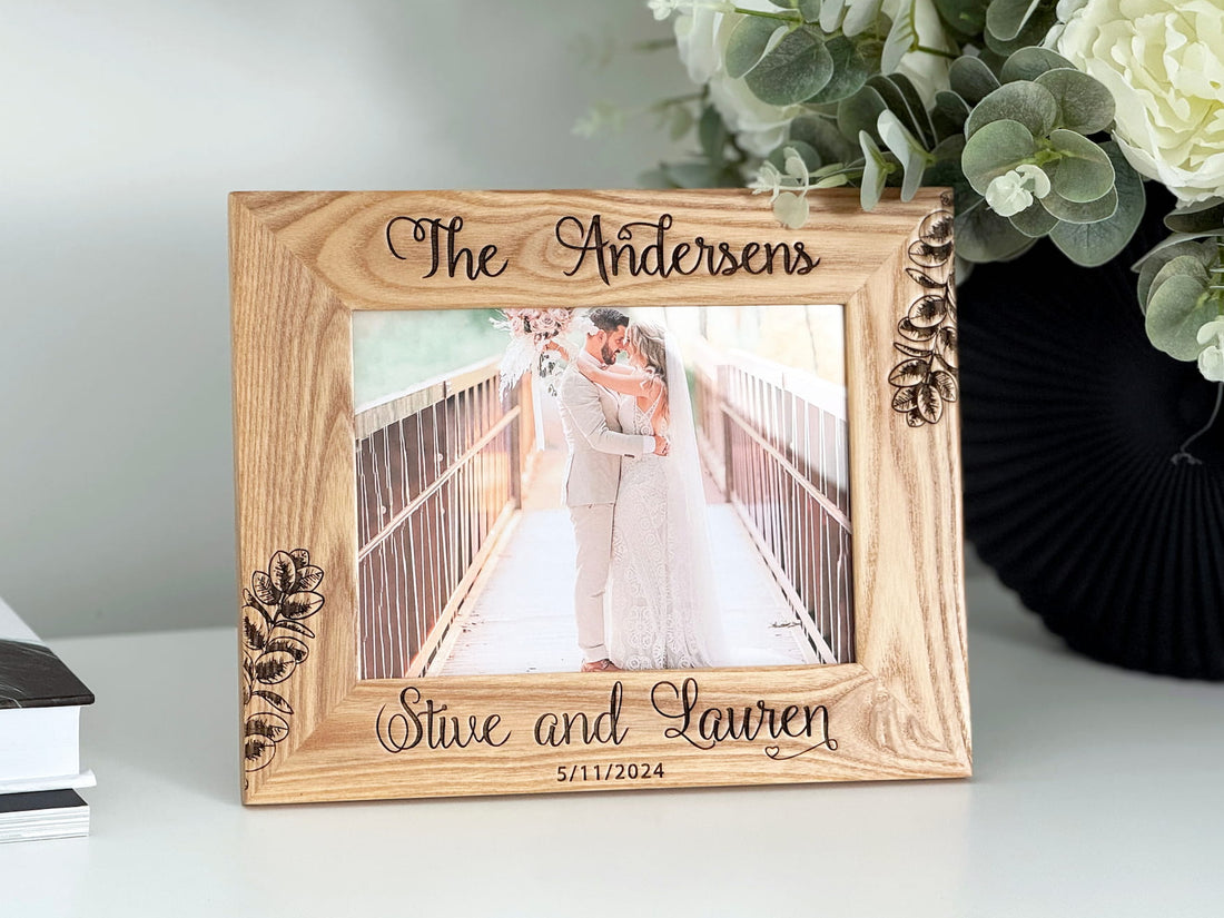 Wooden photo frame with engraved text on a surface with flowers in the background