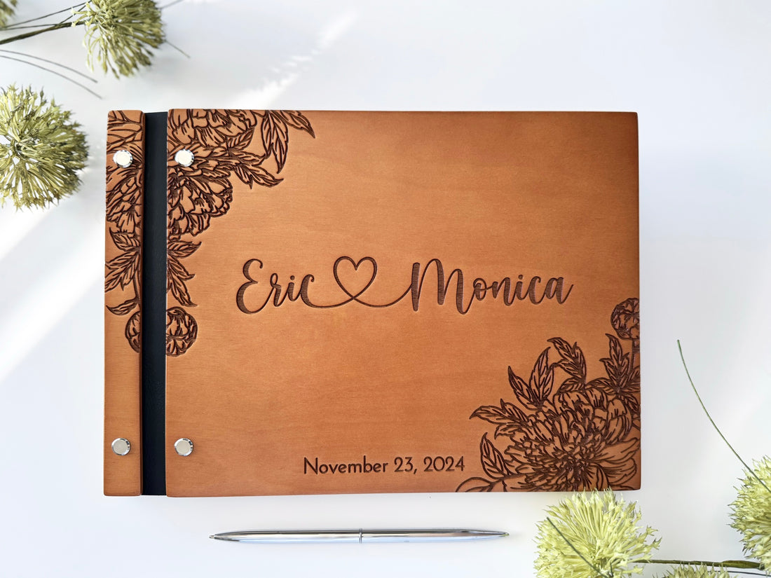 Wooden wedding guest book with names joined by engraved heart and line-art blooms
