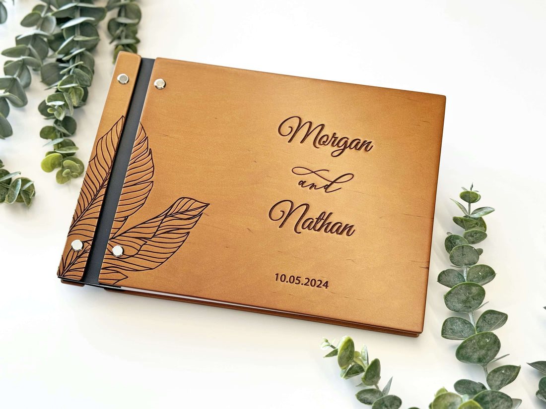 Wooden guest book with engraved names and date, surrounded by greenery