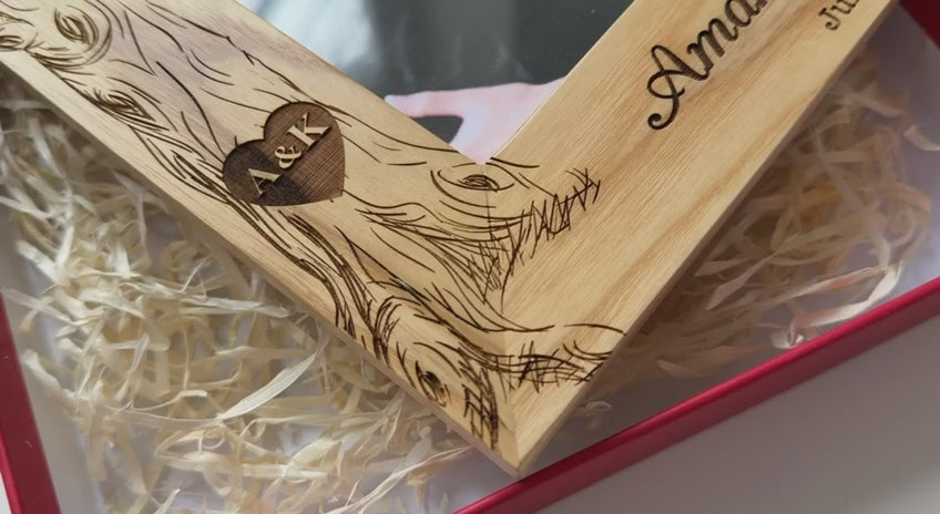 Close-up video of a personalized solid oak picture frame featuring a hand-engraved tree design with names 'Amanda & Kadin' and their wedding date July 15, 2025. The frame is shown inside a red gift box with decorative straw, highlighting the premium wood grain and custom craftsmanship for wedding and anniversary gifting.