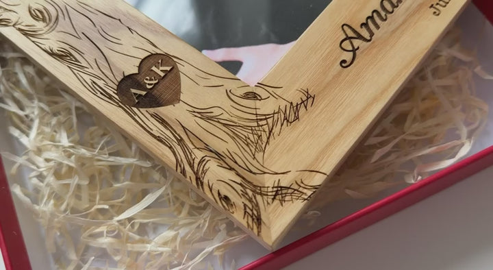 Close-up video of a personalized solid oak picture frame featuring a hand-engraved tree design with names 'Amanda & Kadin' and their wedding date July 15, 2025. The frame is shown inside a red gift box with decorative straw, highlighting the premium wood grain and custom craftsmanship for wedding and anniversary gifting.